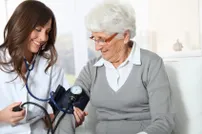 A female healthcare professional measures blood pressure on an elderly woman in a comfortable indoor setting, highlighting patient care.