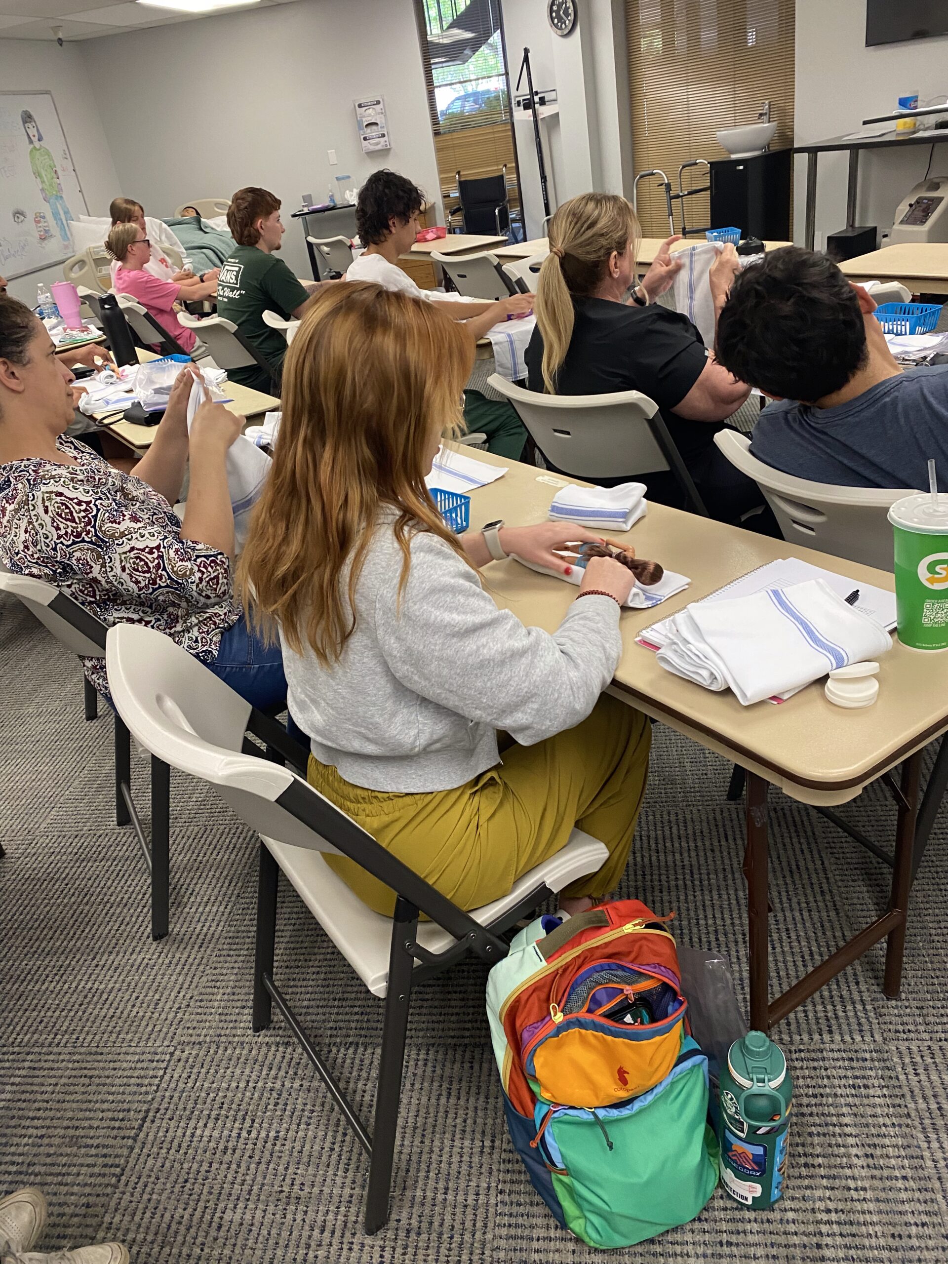 Students participate in a hands-on learning activity in a classroom, focusing on practical skills while seated at desks with materials organized around them.